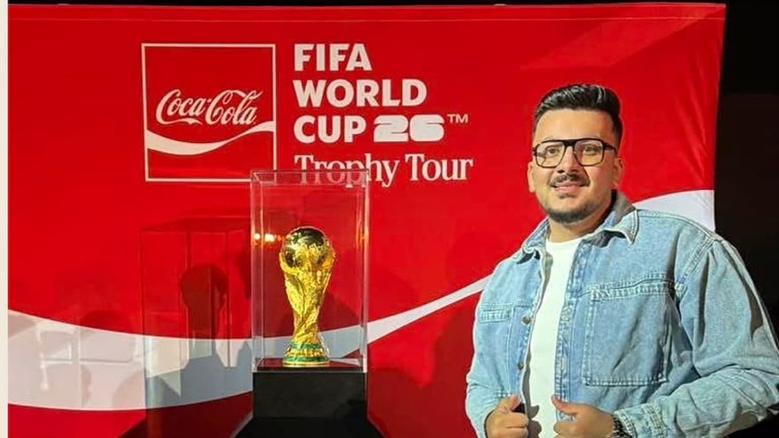 Mohamed Amr Moharez standing beside the FIFA World Cup 26 trophy on its Coca-Cola Trophy Tour display.